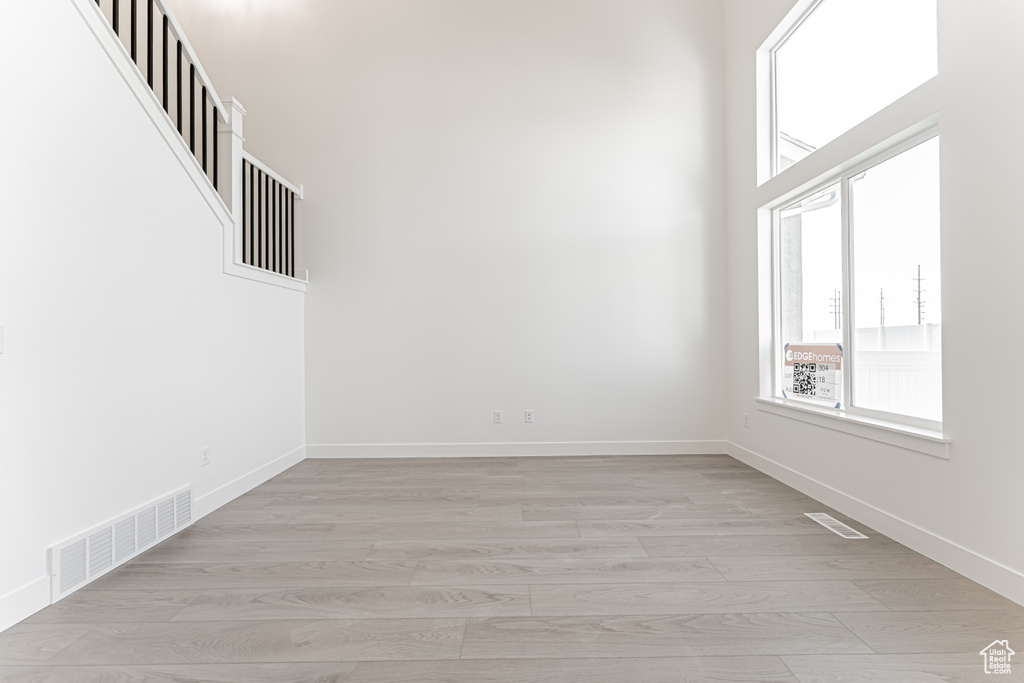 Spare room featuring plenty of natural light, light wood-type flooring, baseboards, and a high ceiling