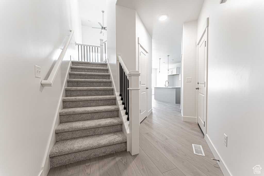 Stairway with a ceiling fan, wood finished floors, and baseboards