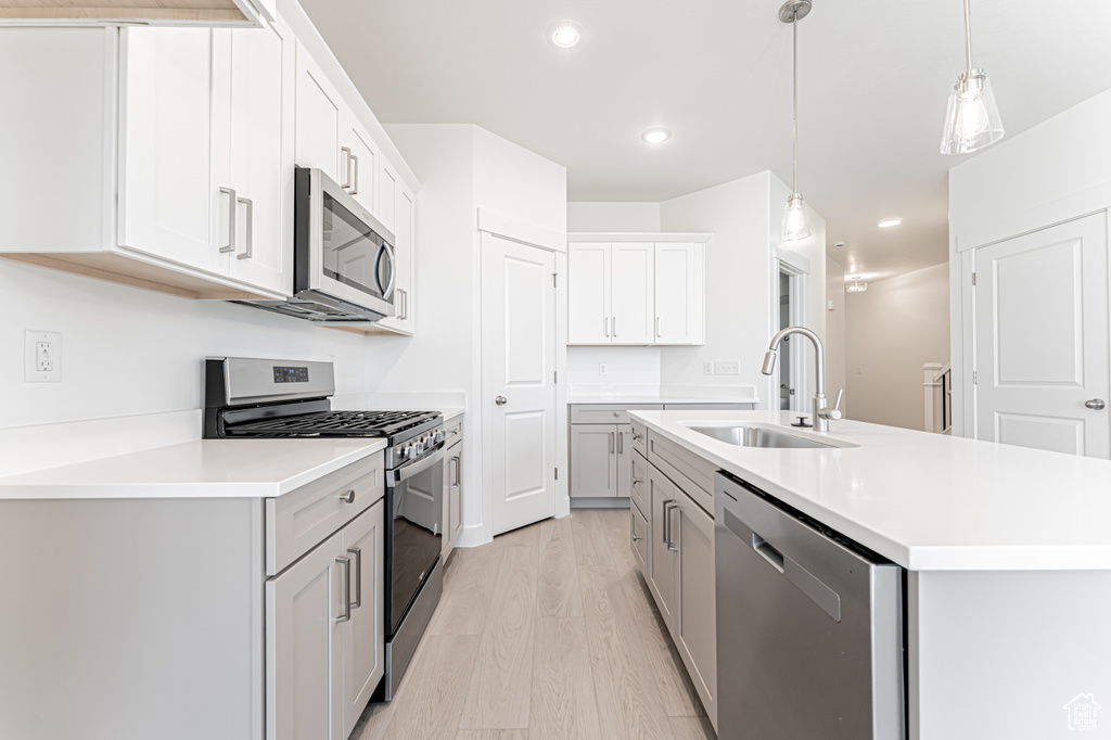 Kitchen featuring stainless steel appliances, a sink, a center island with sink, light countertops, and recessed lighting