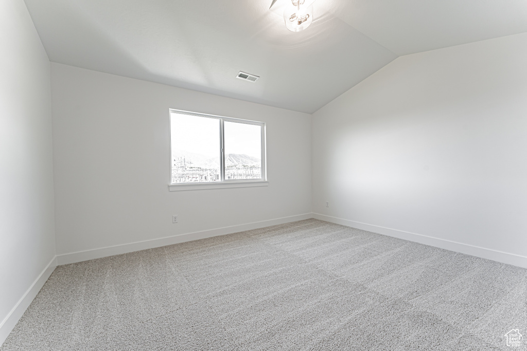 Carpeted spare room featuring vaulted ceiling and baseboards