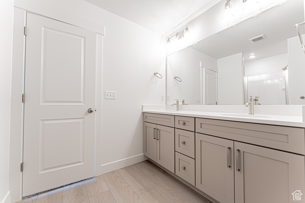 Bathroom featuring double vanity, baseboards, a shower, and wood finished floors