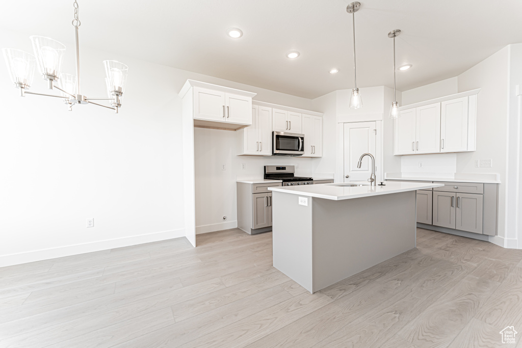Kitchen with appliances with stainless steel finishes, a chandelier, light wood-style flooring, a sink, and baseboards