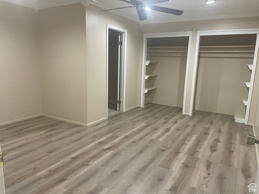 Unfurnished bedroom featuring ceiling fan, light wood-type flooring, crown molding, and two closets