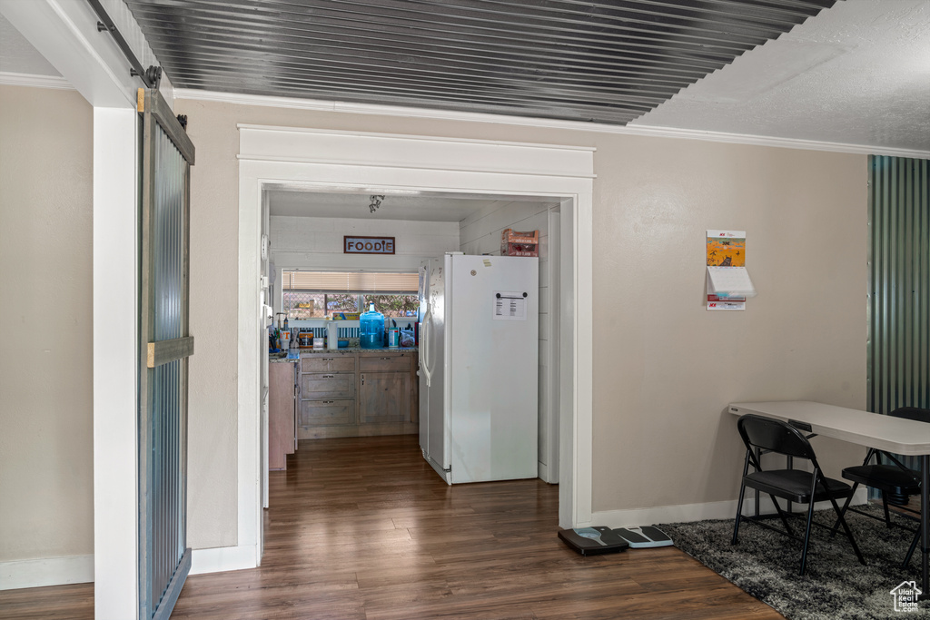 Hallway featuring baseboards, a barn door, dark wood-style flooring, and crown molding