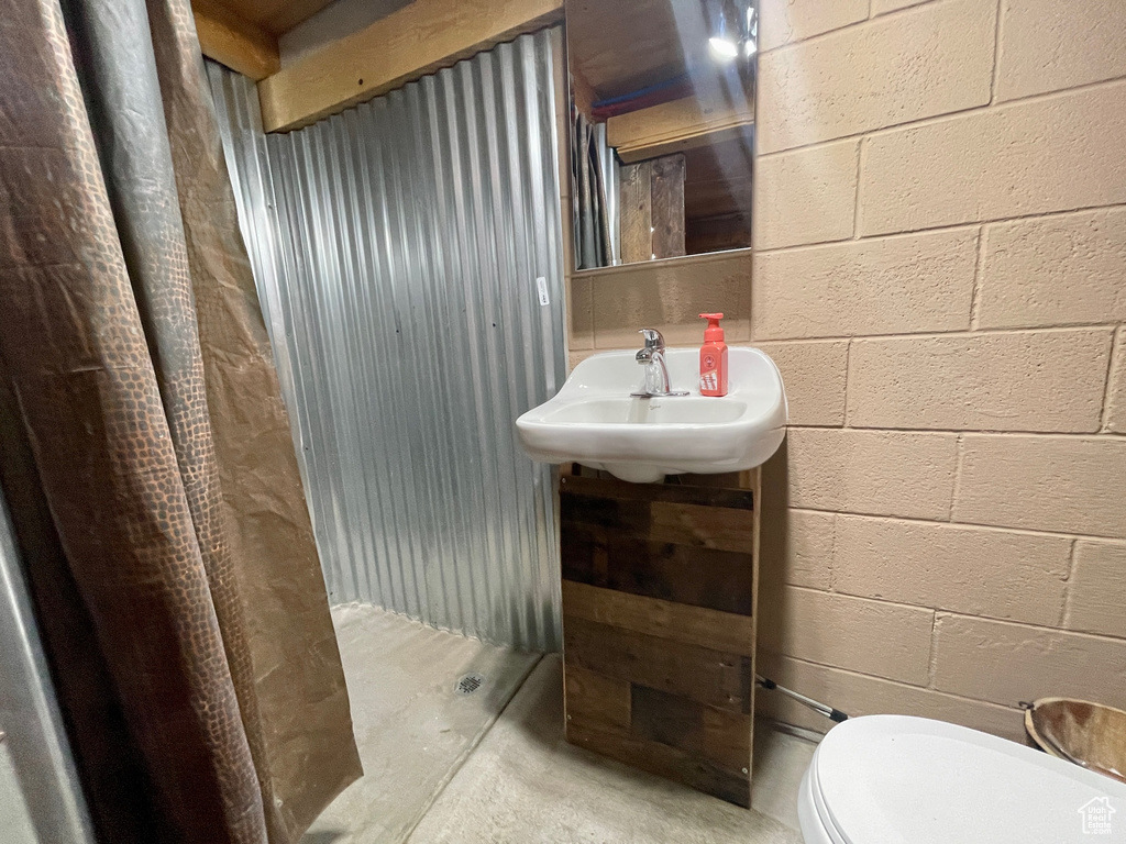 Half bath with concrete flooring, concrete block wall, a sink, and toilet