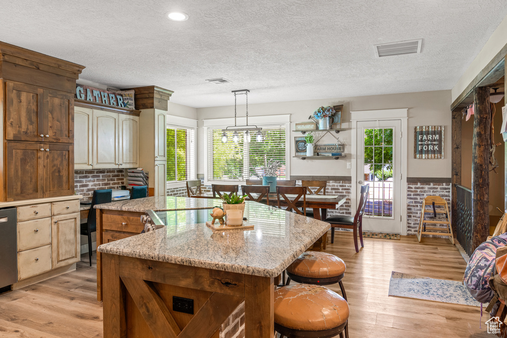 Kitchen featuring hanging light fixtures, a center island, light hardwood / wood-style floors, and light stone counters