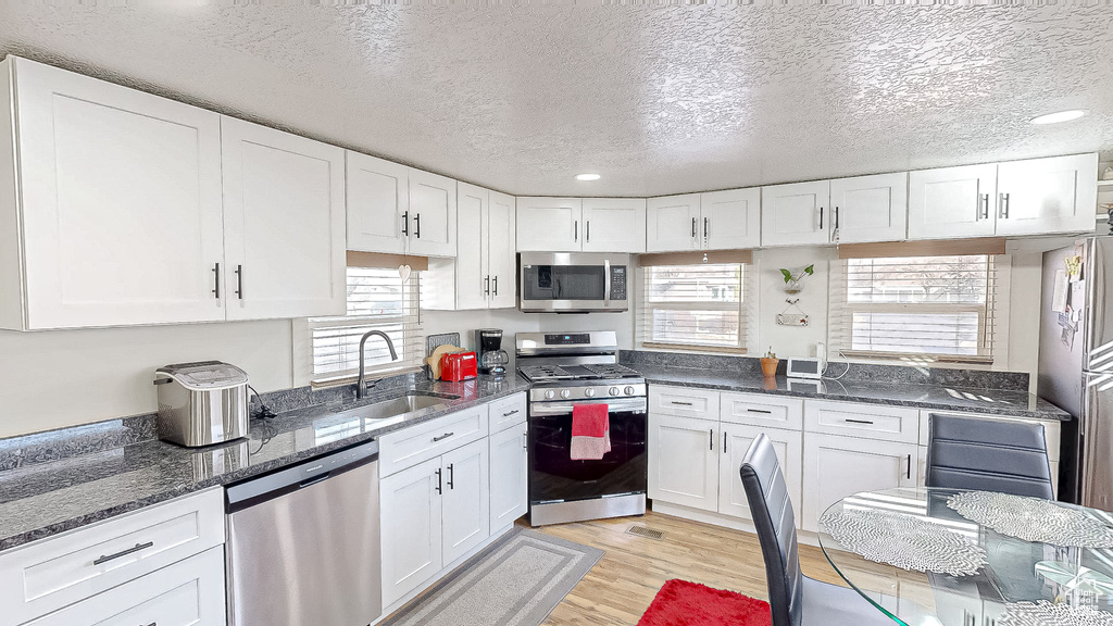 Kitchen featuring sink, plenty of natural light, stainless steel appliances, light hardwood / wood-style floors, and white cabinets