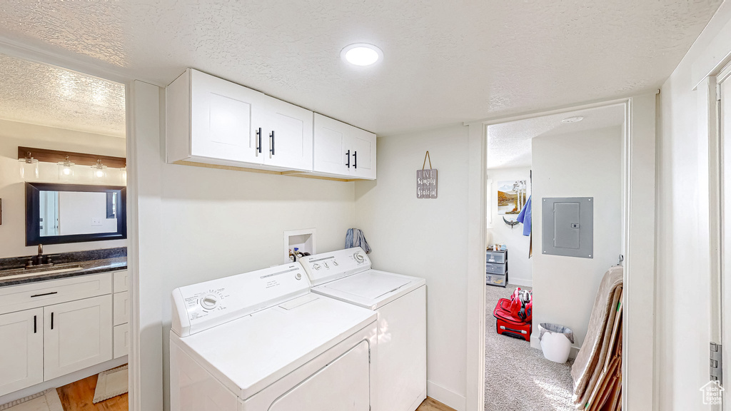 Laundry room with sink, electric panel, washer and dryer, a textured ceiling, and light carpet