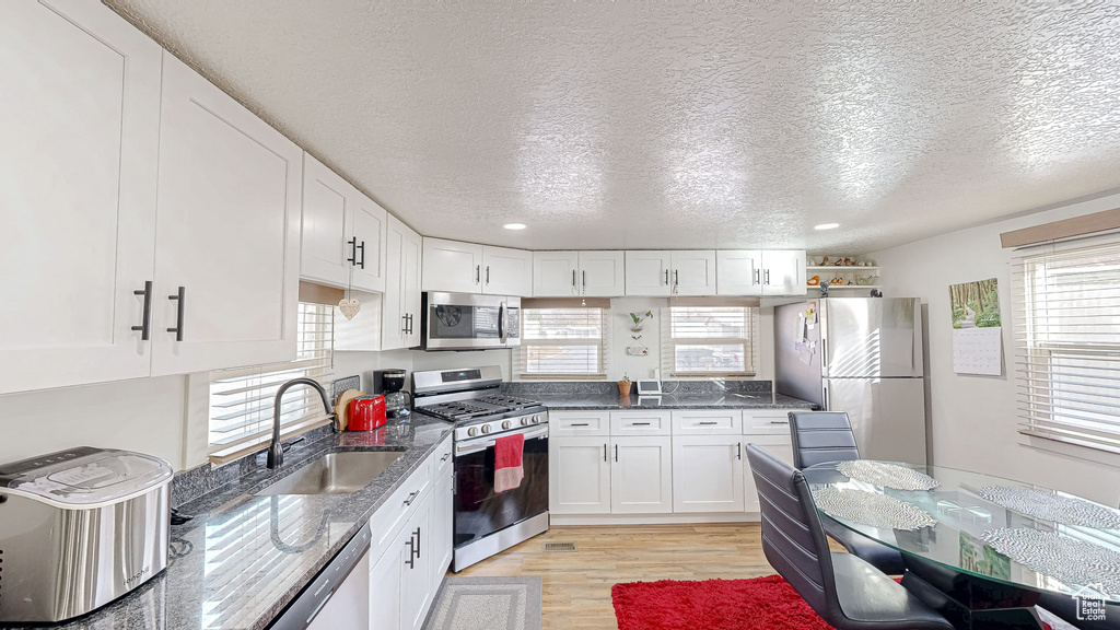 Kitchen featuring white cabinetry, sink, dark stone counters, stainless steel appliances, and light hardwood / wood-style flooring