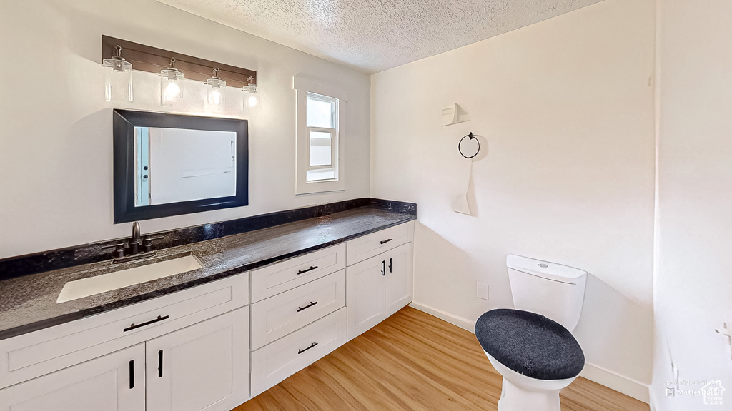 Bathroom with a textured ceiling, toilet, wood finished floors, vanity, and baseboards