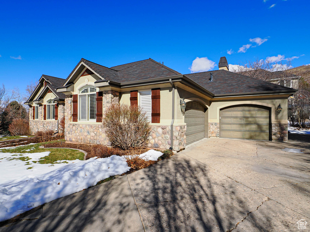 View of front of home with a garage, stone siding, concrete driveway, and stucco siding