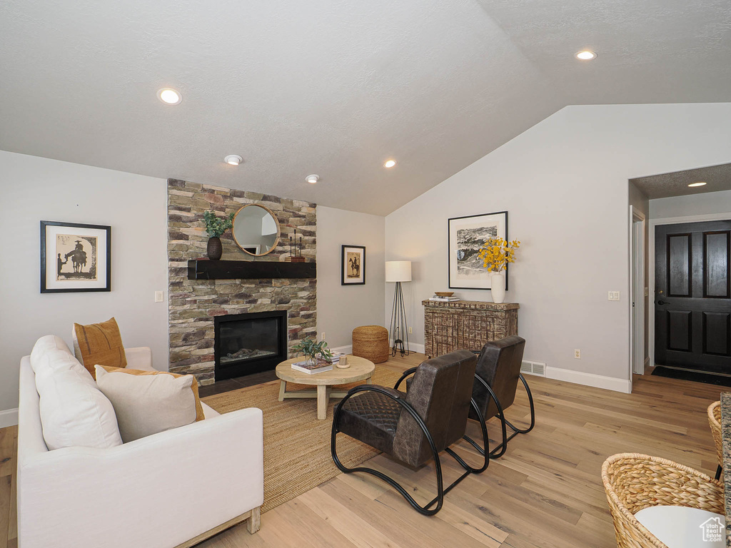 Living room with a fireplace, visible vents, baseboards, vaulted ceiling, and light wood-style floors