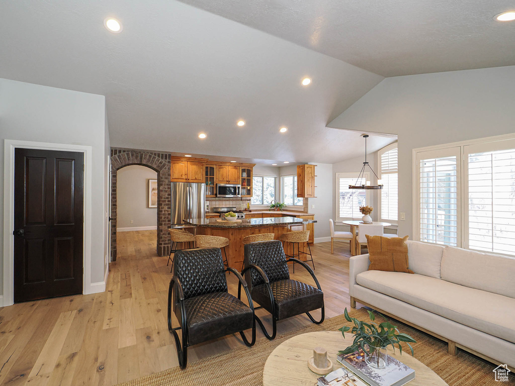 Living area with light wood-style flooring, arched walkways, lofted ceiling, and recessed lighting