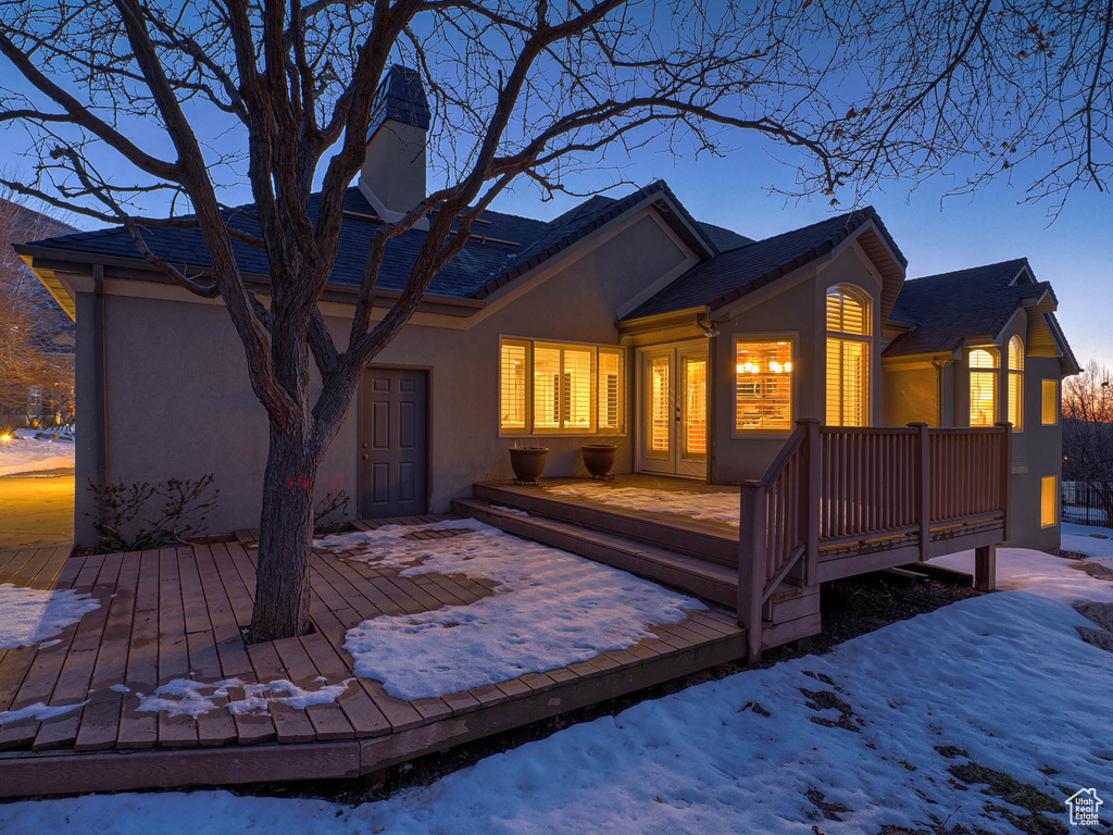 Snow covered rear of property with french doors, a deck, and stucco siding