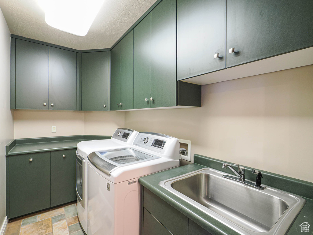 Laundry area featuring cabinet space, independent washer and dryer, stone finish flooring, a textured ceiling, and a sink