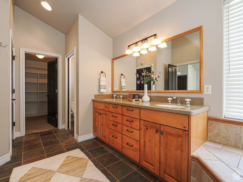 Full bathroom with double vanity, a spacious closet, vaulted ceiling, and a sink