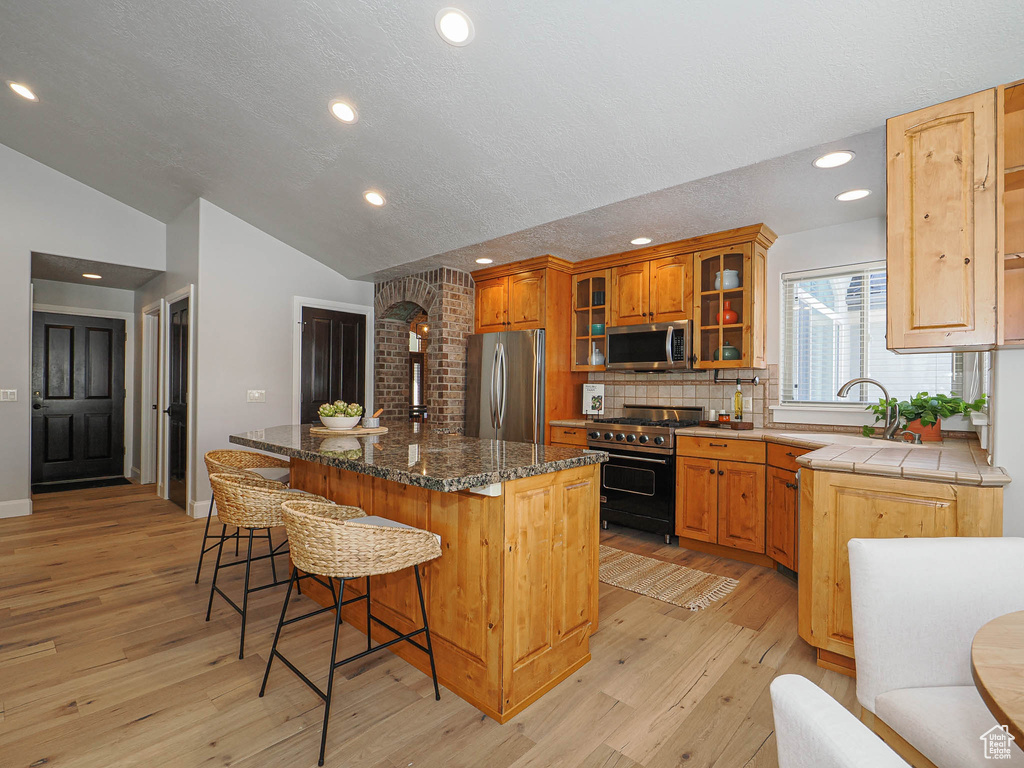 Kitchen featuring lofted ceiling, a kitchen island, glass insert cabinets, a breakfast bar area, and stainless steel appliances