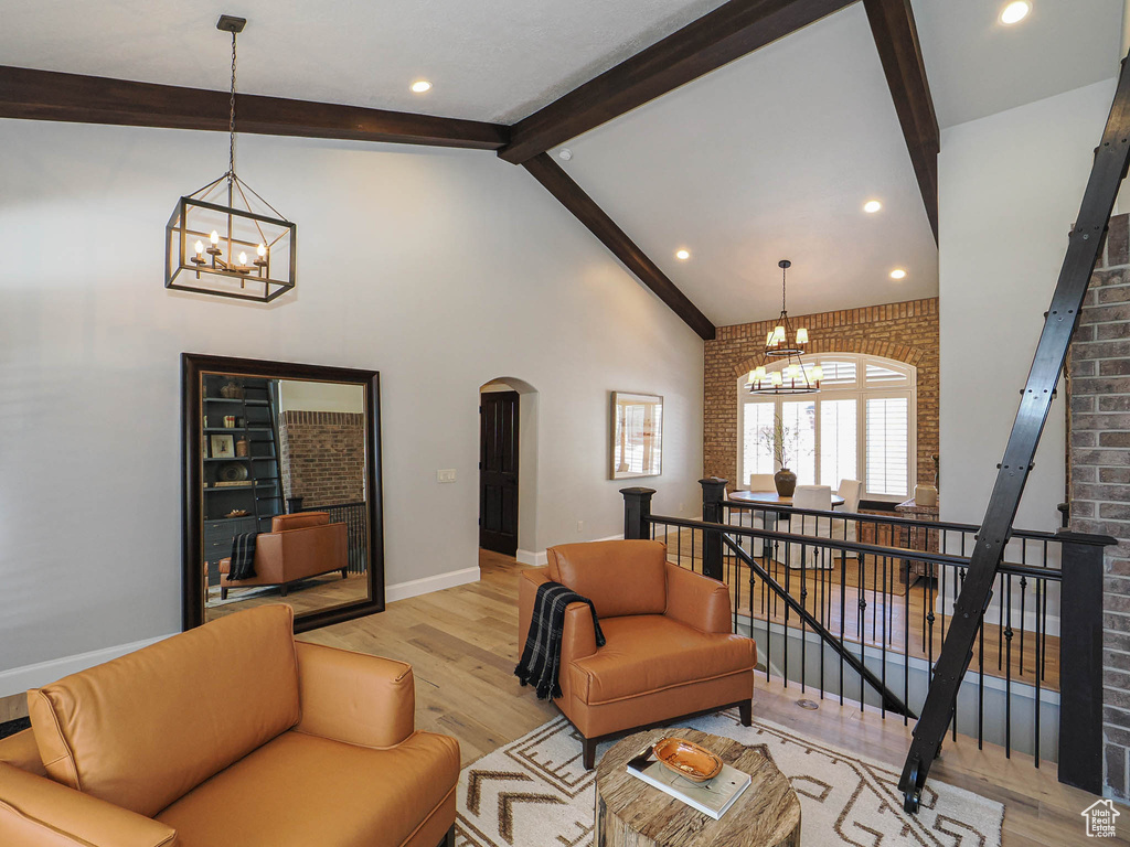 Living room with a chandelier, arched walkways, light wood-style flooring, brick wall, and beam ceiling