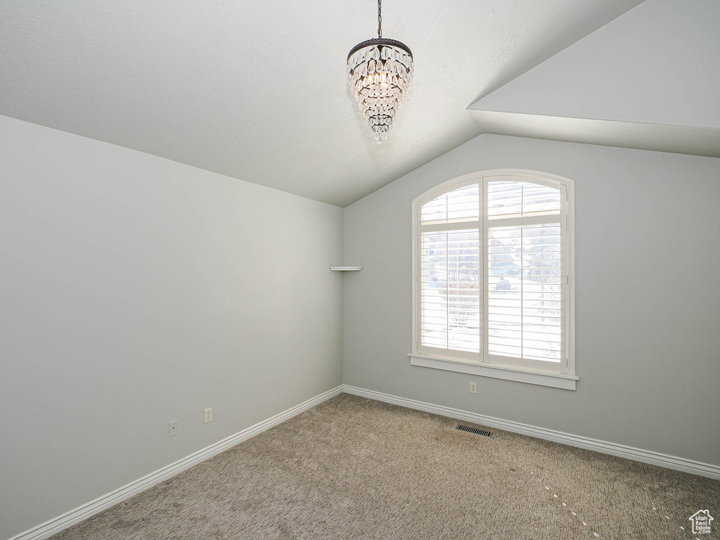 Unfurnished room featuring visible vents, an inviting chandelier, carpet flooring, vaulted ceiling, and baseboards