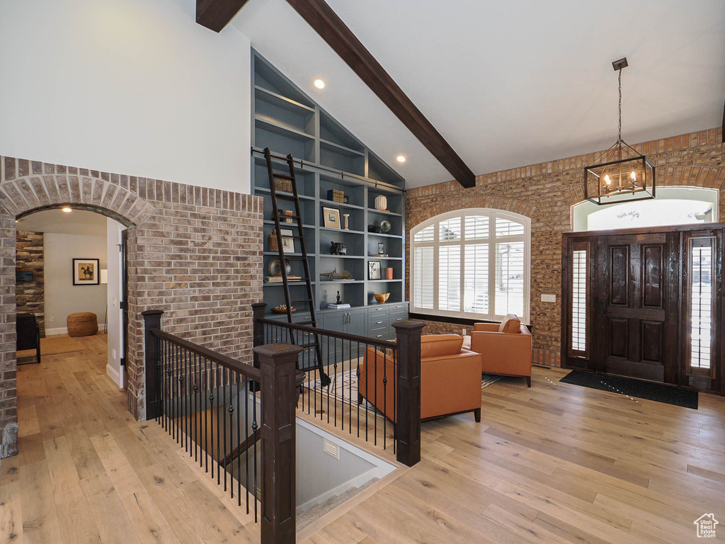 Entryway with light wood finished floors, high vaulted ceiling, arched walkways, and beamed ceiling