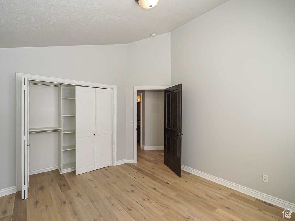 Unfurnished bedroom featuring light wood finished floors, baseboards, vaulted ceiling, a textured ceiling, and a closet