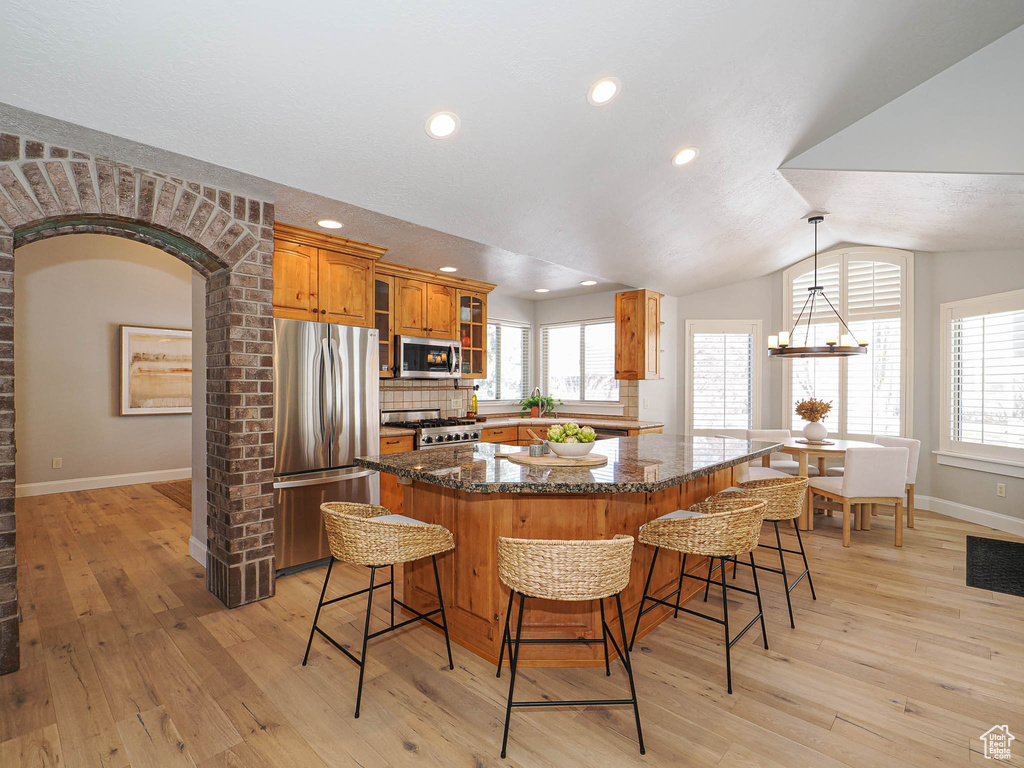 Kitchen with appliances with stainless steel finishes, a kitchen bar, glass insert cabinets, and brown cabinets