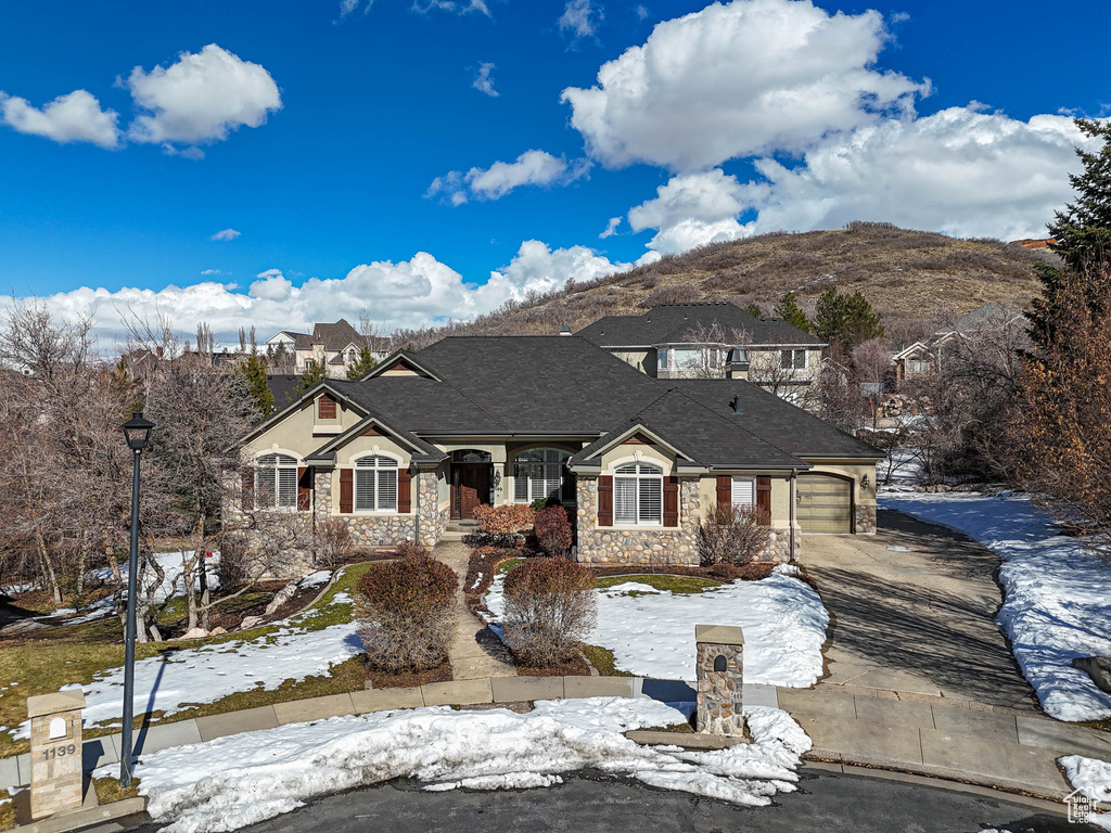 French provincial home featuring a garage, a shingled roof, concrete driveway, stone siding, and a mountain view