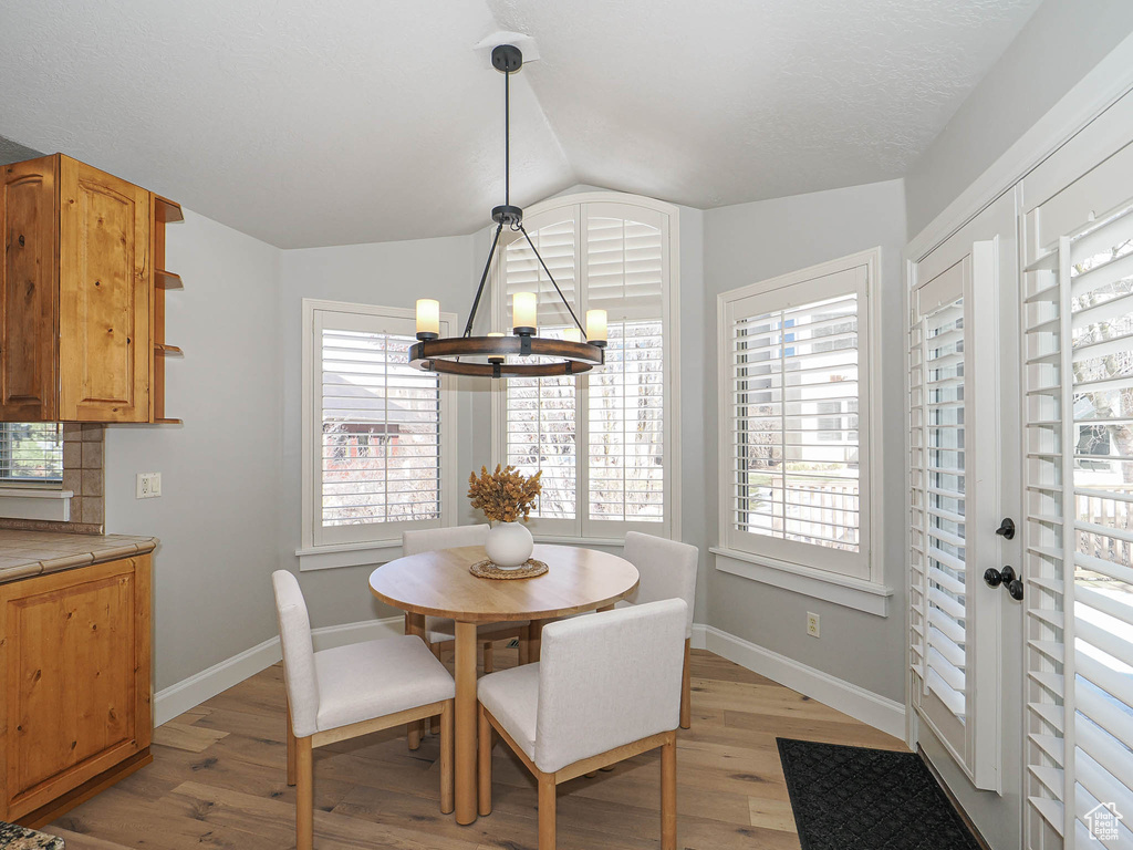 Dining room with baseboards, vaulted ceiling, light wood finished floors, and an inviting chandelier