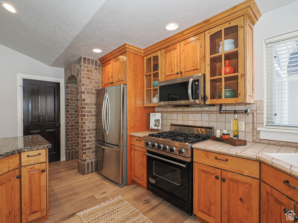 Kitchen with glass insert cabinets, light wood finished floors, appliances with stainless steel finishes, and brown cabinets