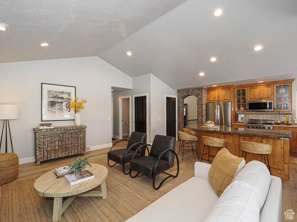 Living room featuring light wood-style floors, arched walkways, vaulted ceiling, and a textured ceiling