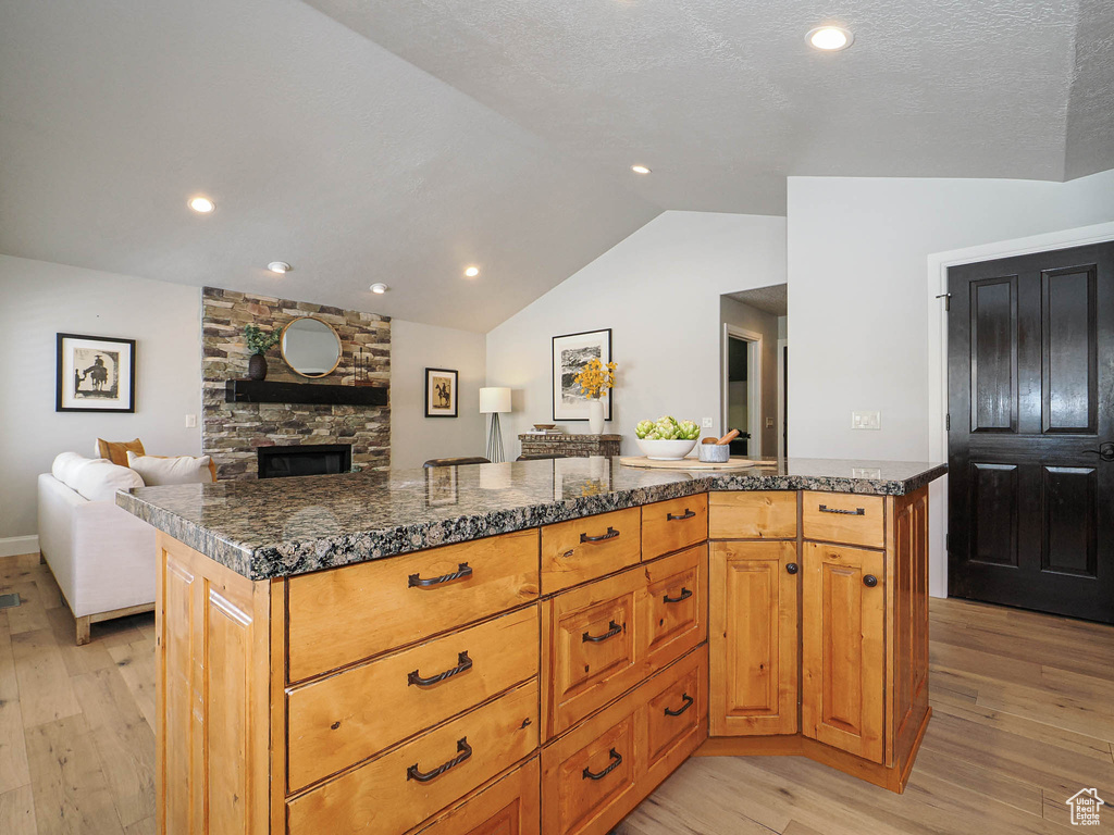 Kitchen featuring light wood-style flooring, a kitchen island, open floor plan, vaulted ceiling, and a fireplace