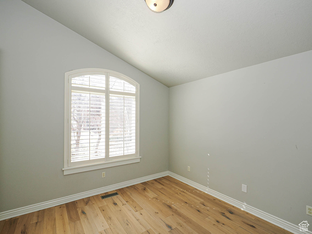 Spare room featuring vaulted ceiling, light wood-type flooring, visible vents, and baseboards