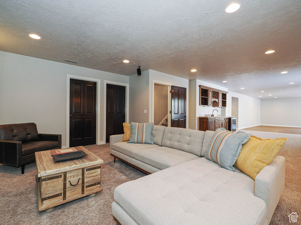 Carpeted living room with baseboards, stairway, wet bar, a textured ceiling, and recessed lighting