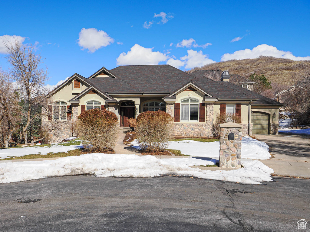 View of front of home with a garage, stone siding, driveway, and a chimney