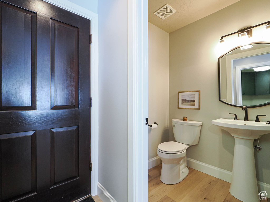 Half bath with visible vents, toilet, a sink, wood finished floors, and baseboards