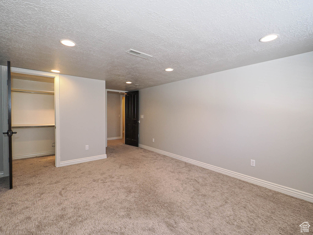 Interior space featuring light carpet, baseboards, visible vents, a walk in closet, and a textured ceiling
