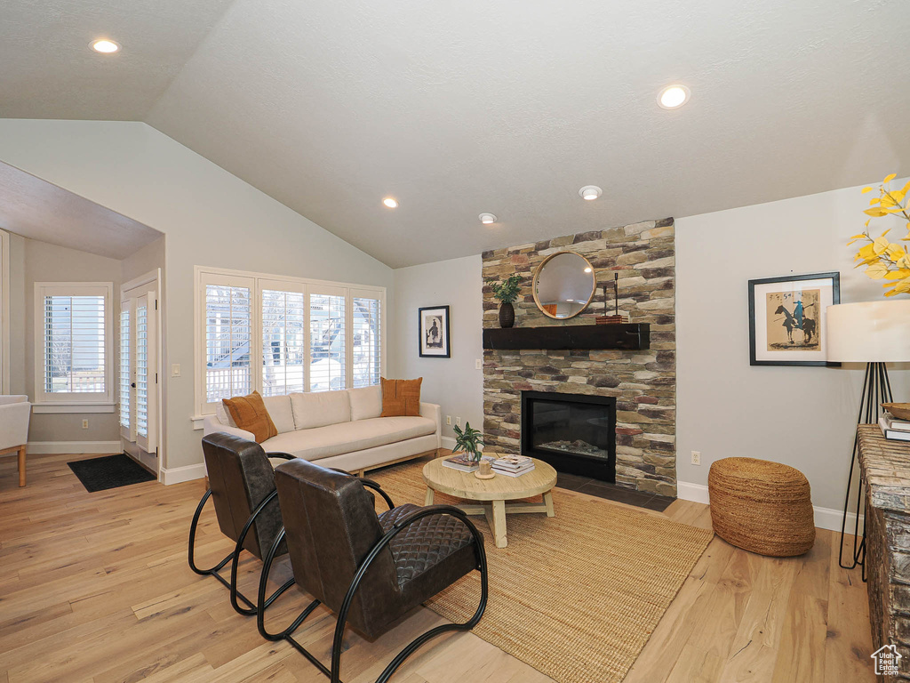 Living room featuring lofted ceiling, light wood-type flooring, a fireplace, and baseboards
