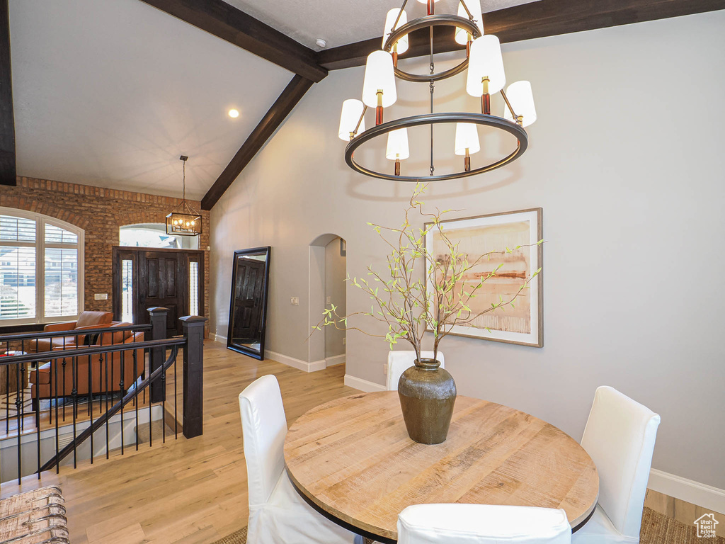 Dining space featuring baseboards, arched walkways, light wood-style flooring, a notable chandelier, and beam ceiling