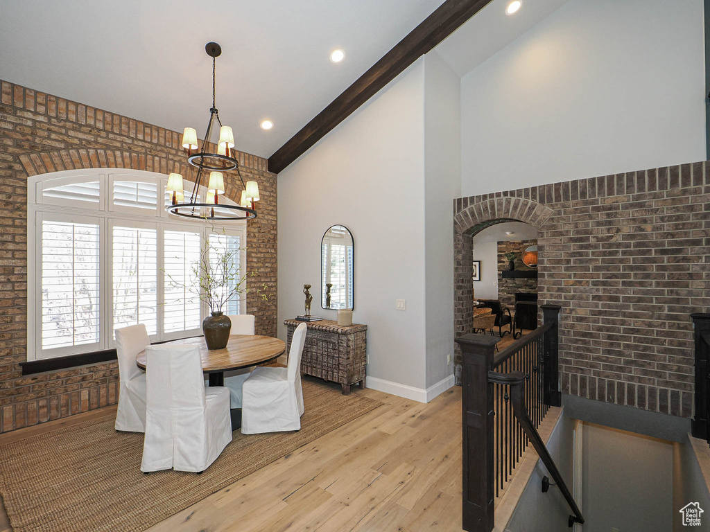 Dining area with high vaulted ceiling, light wood-type flooring, beamed ceiling, and brick wall