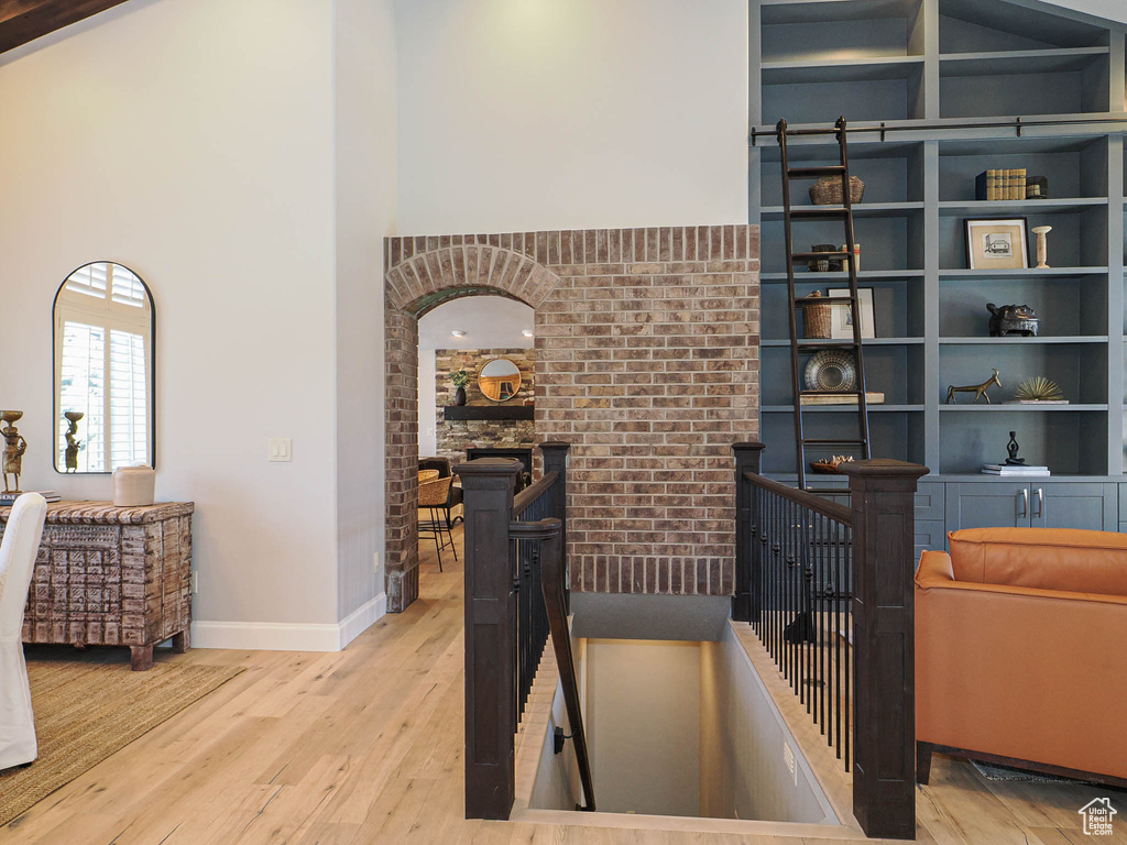 Interior space featuring built in shelves, brick wall, wood finished floors, a towering ceiling, and baseboards