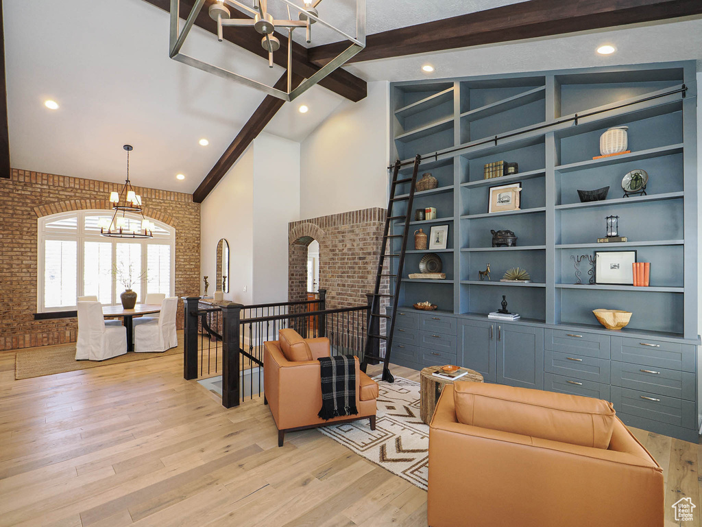 Sitting room featuring a chandelier, high vaulted ceiling, brick wall, an upstairs landing, and light wood-style floors