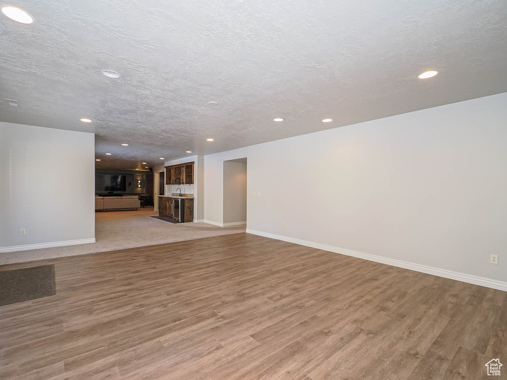 Unfurnished living room featuring a textured ceiling, light wood-type flooring, and baseboards