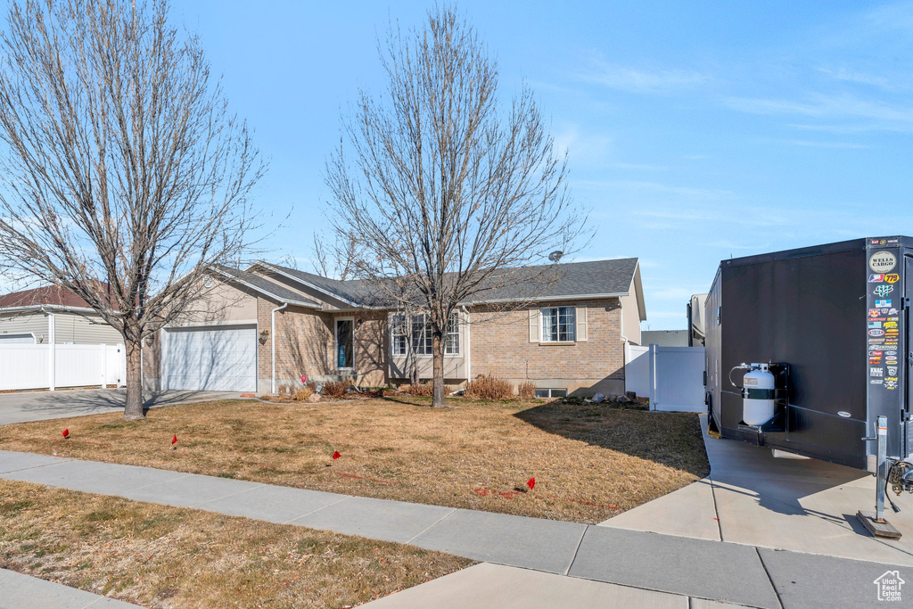 View of front of home with a garage, brick siding, fence, driveway, and a front lawn