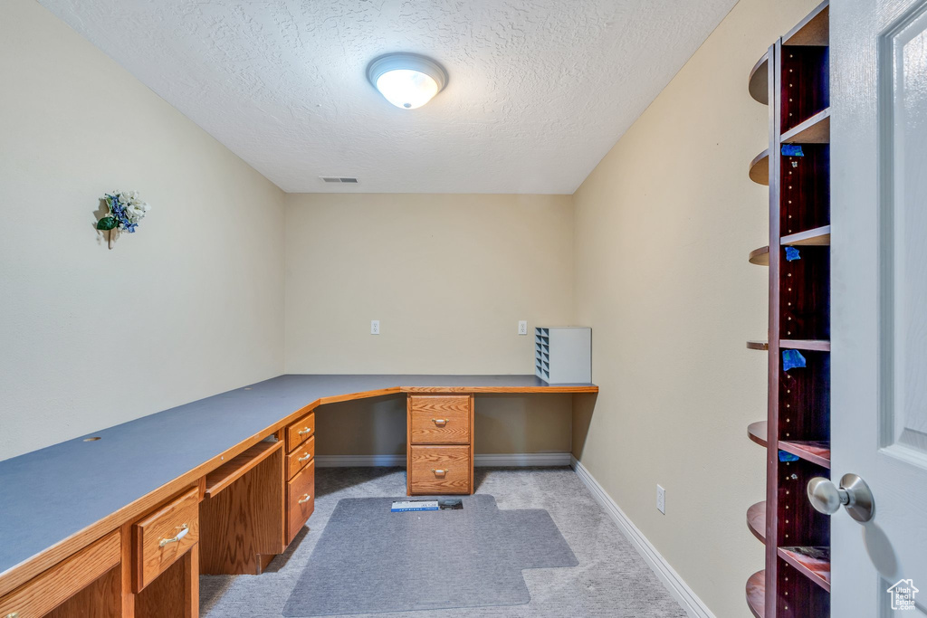 Office space with a textured ceiling, light carpet, visible vents, baseboards, and built in study area