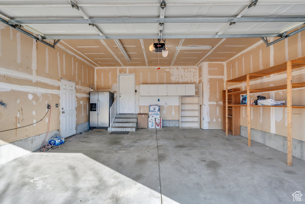 Garage featuring a garage door opener and stainless steel fridge