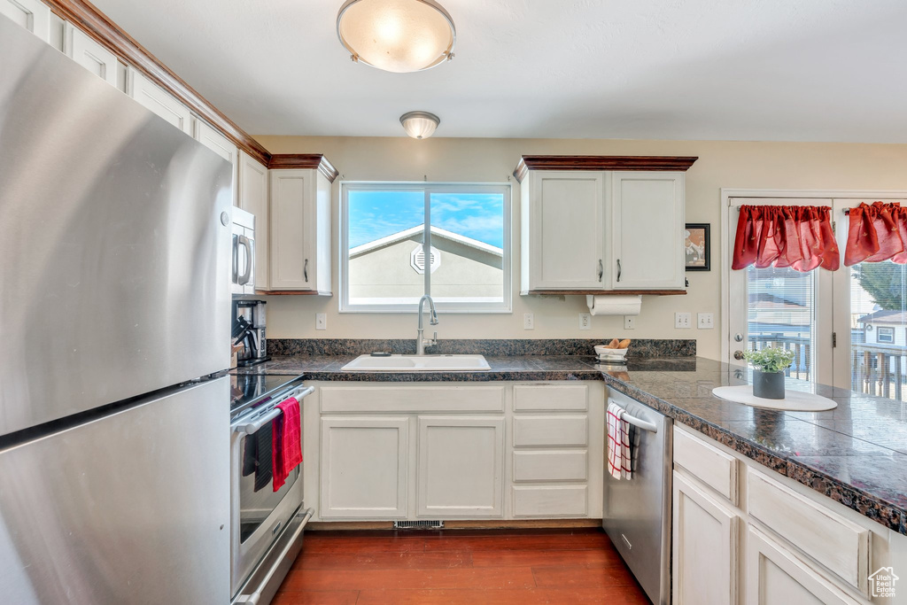 Kitchen with dark wood-type flooring, appliances with stainless steel finishes, white cabinets, and a sink