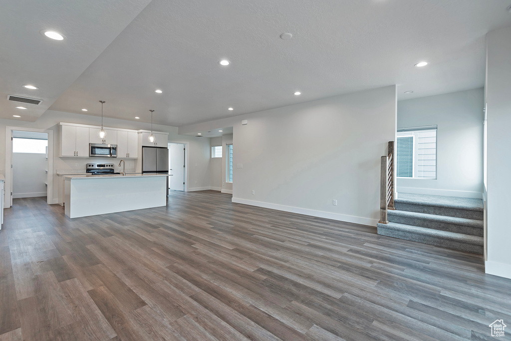 Unfurnished living room with recessed lighting, dark wood-style flooring, visible vents, and stairway