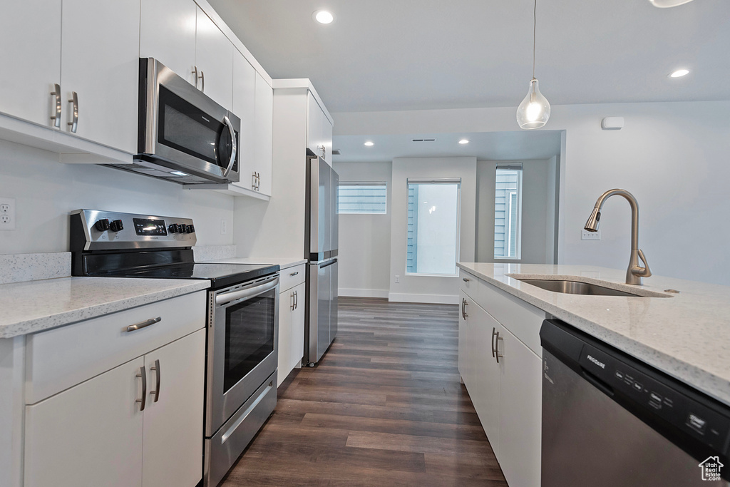 Kitchen with a sink, white cabinetry, hanging light fixtures, appliances with stainless steel finishes, and light stone countertops