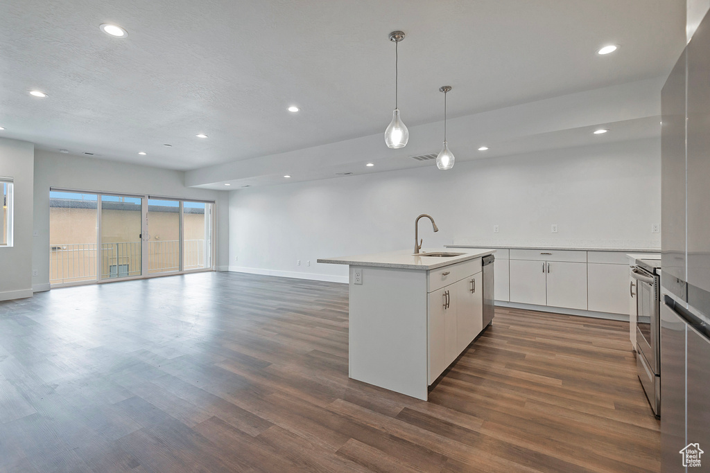 Kitchen featuring a center island with sink, white cabinets, stainless steel appliances, light countertops, and a sink