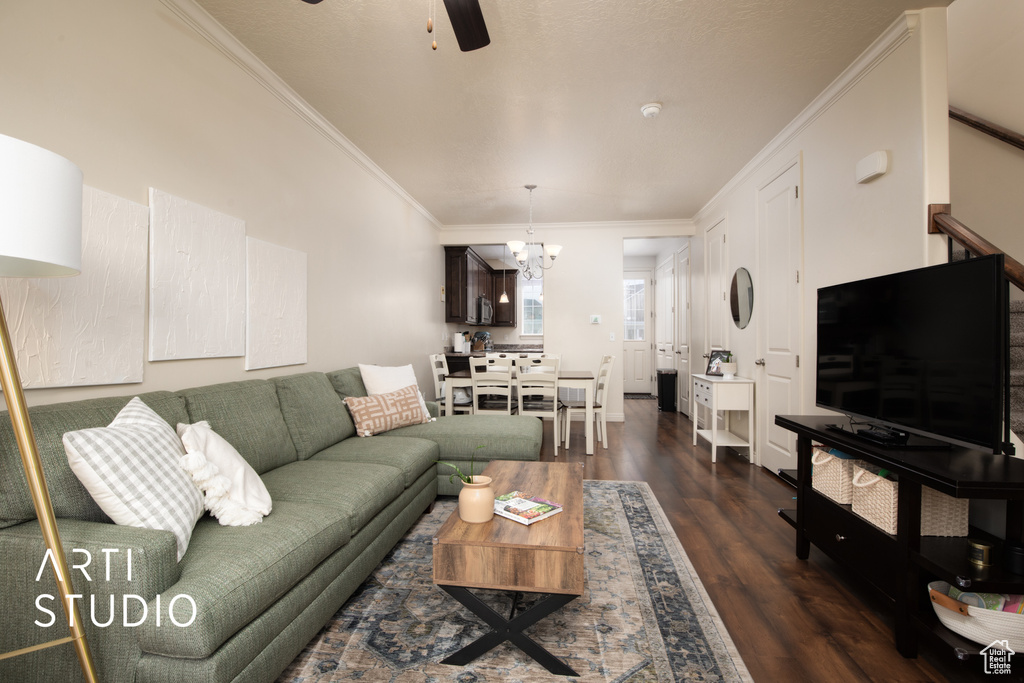 Living area with ornamental molding, dark wood finished floors, stairway, and ceiling fan with notable chandelier
